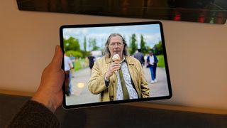 The 13-inch iPad Air being held in one hand. On the screen is an image from Slow Horses.