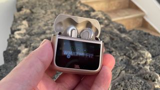 JBL Tour Pro 3 noise cancelling earbuds in case held in hand above stone wall